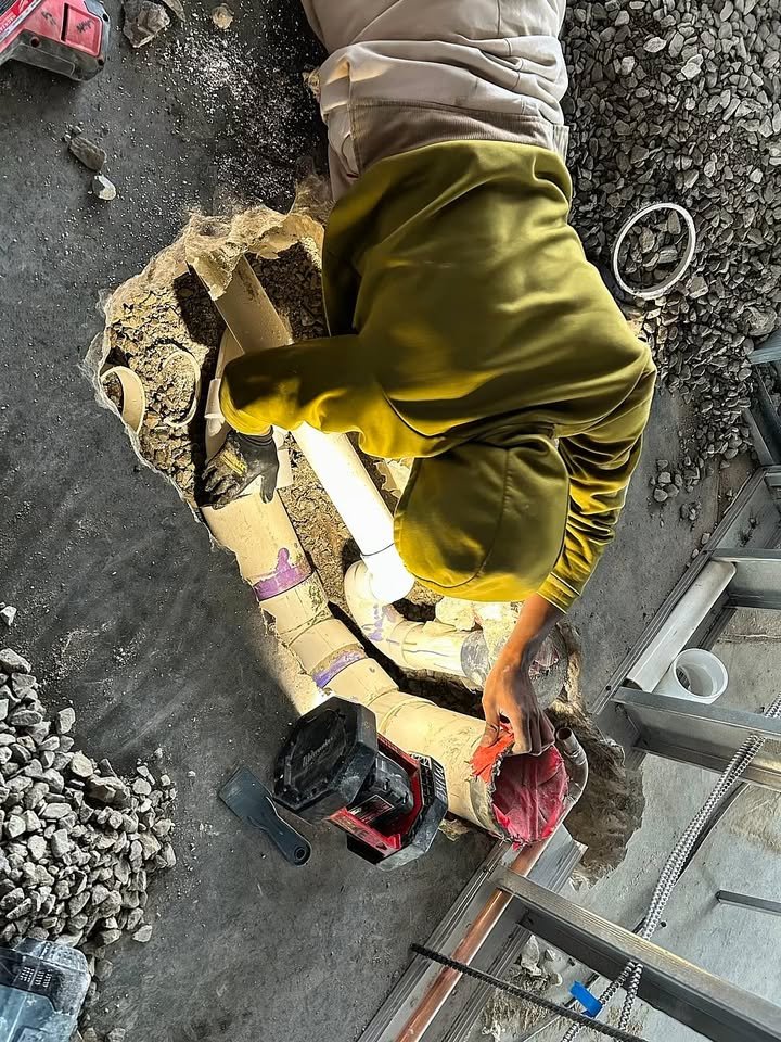 A Just Plumbing technician working on new PVC drain pipe in an opened concrete floor